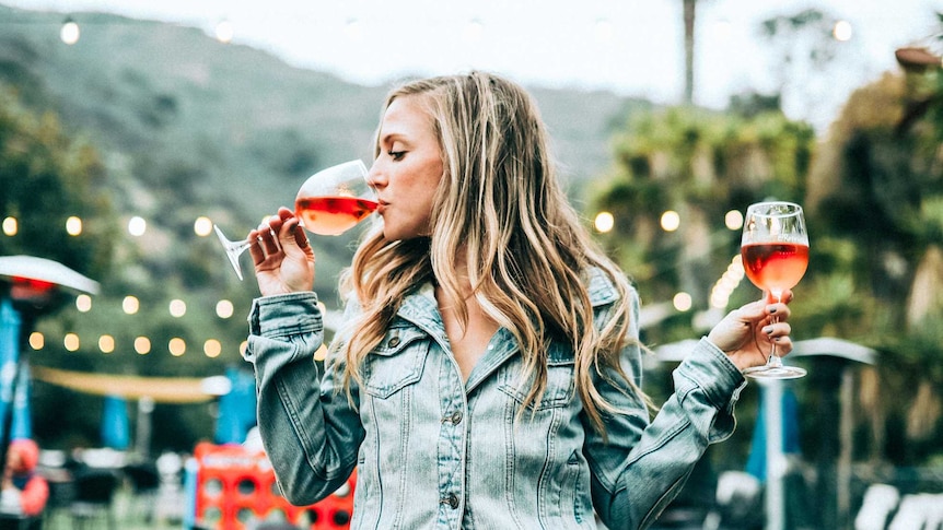 A young woman who takes two glasses of wine and drinks from one to talk about the dangers of casual drinking.