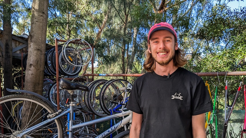 Andrew Stark smiling wearing a pink cap and black tee standing in front a rack of bikes