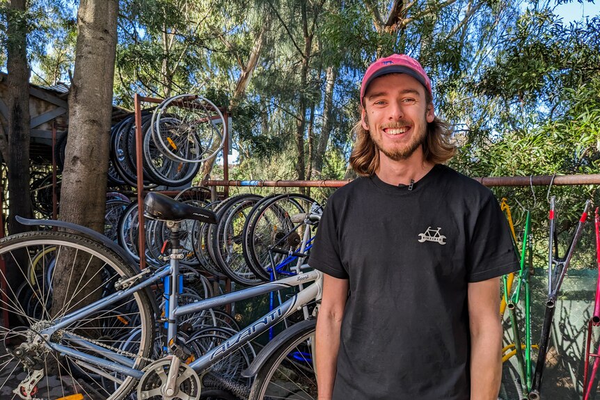 Andre Stark smiling wearing a pink cap and black tee standing in front a rack of bikes