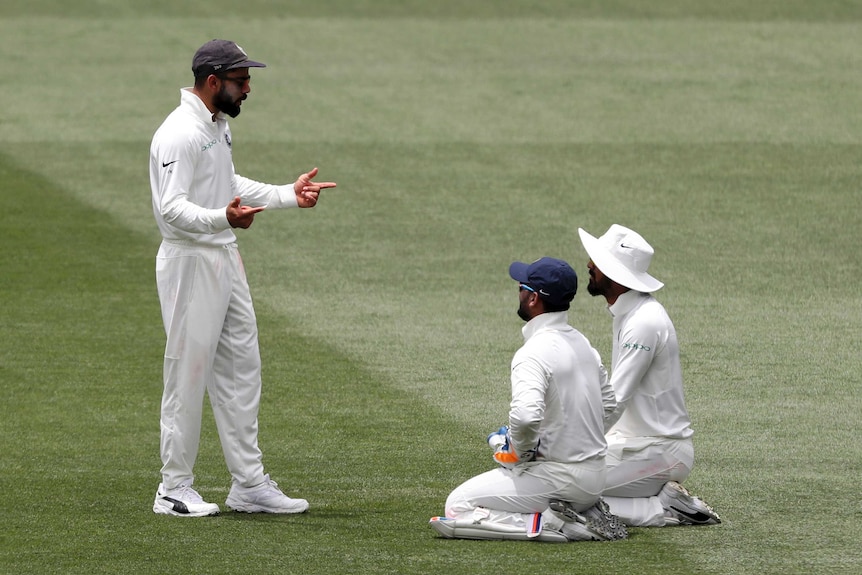 Indian captain Virat Kohli speaks to teammates Rishabh Pant and KL Rahul, both kneeling, during a day of Test cricket.