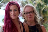 A woman with tattoos and long red hair with an older woman with blonde hair and glasses