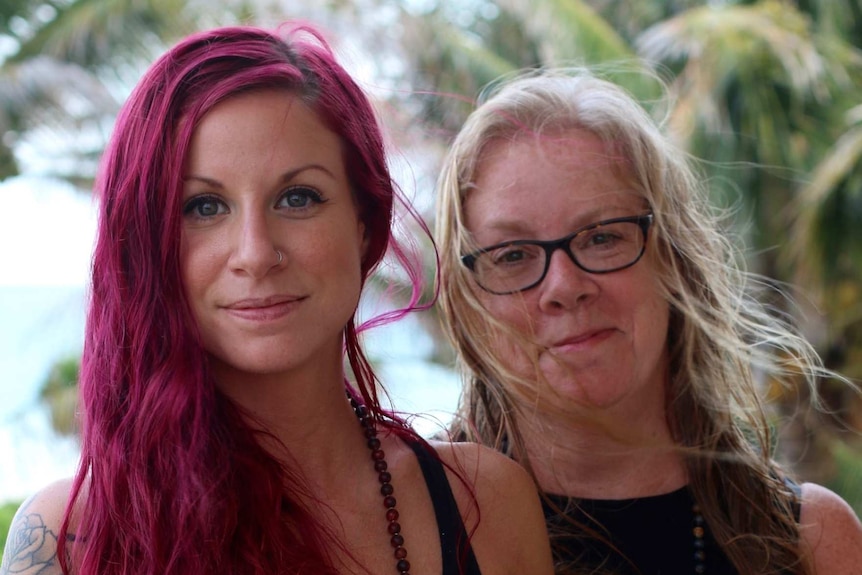 A woman with tattoos and long red hair with an older woman with blonde hair and glasses