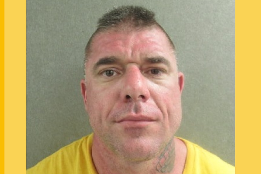 A man with short hair and a neck tattoo appears in a police mugshot wanted poster