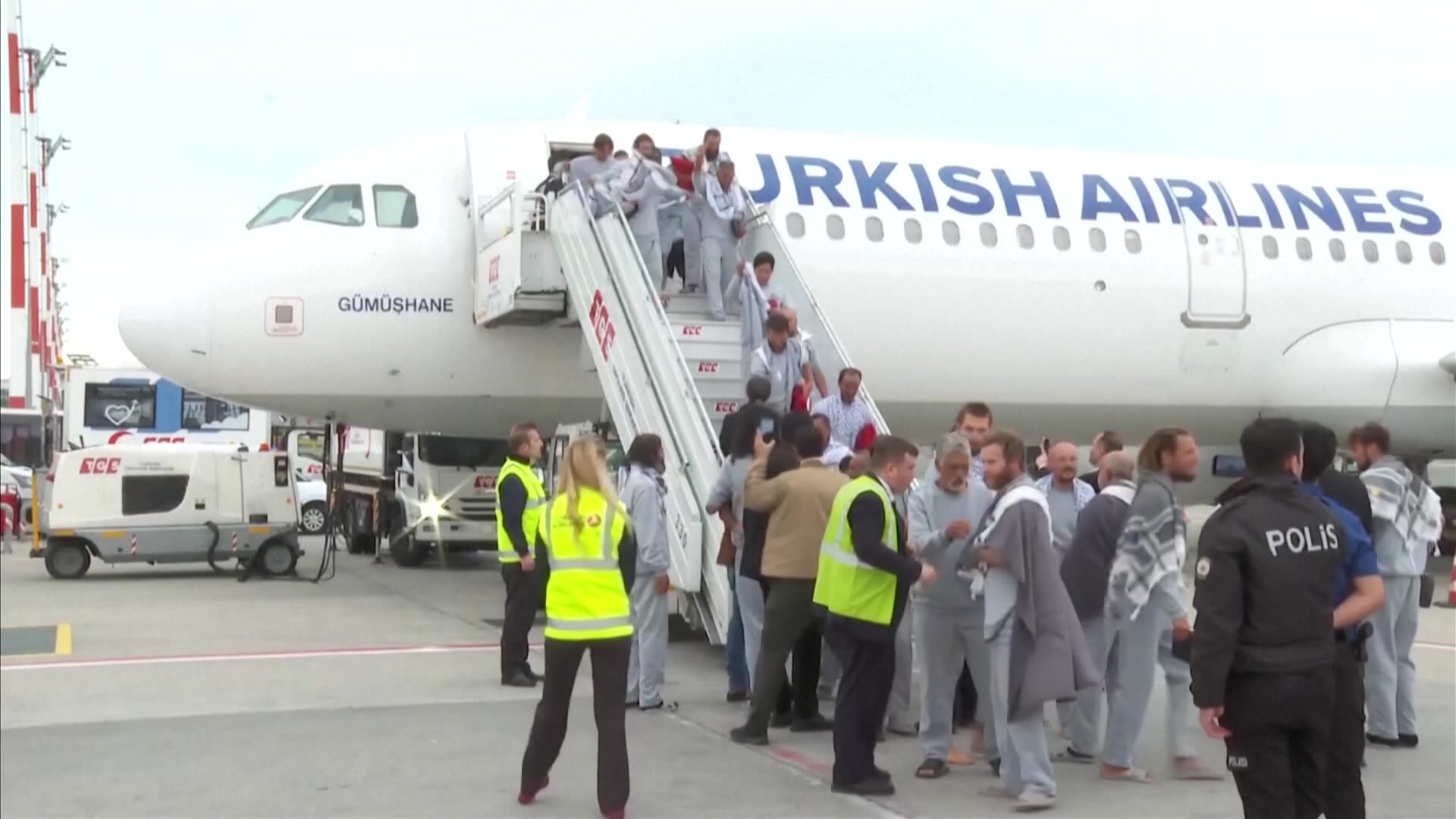 Turkish Airlines plane with people disembarking down the stairs at the from of the plane. The people are wearing grey tracksuits