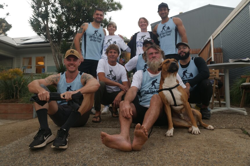 A group of runners in blue singlets sit with a dog outside a homeless service