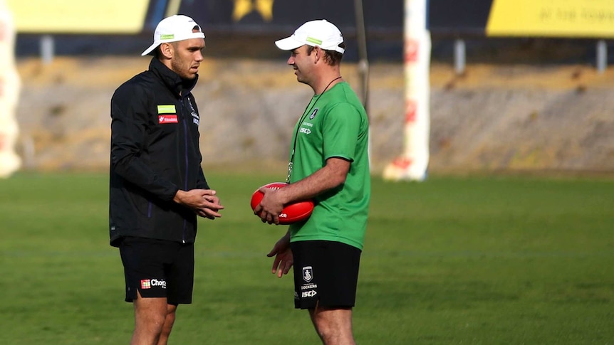 AFL footballer Harley Bennell talks to a trainer holding a football on an oval
