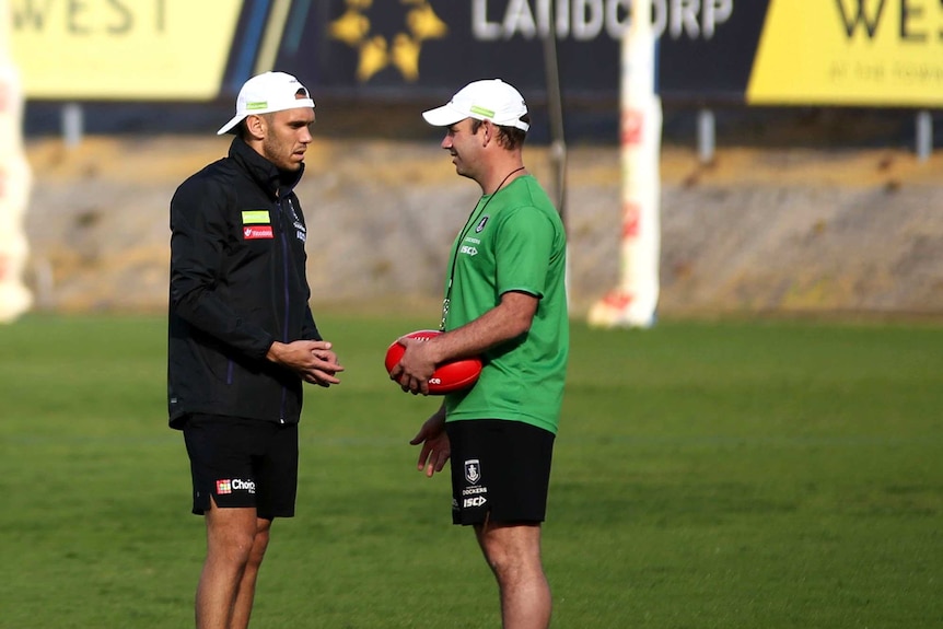 AFL footballer Harley Bennell talks to a trainer holding a football on an oval