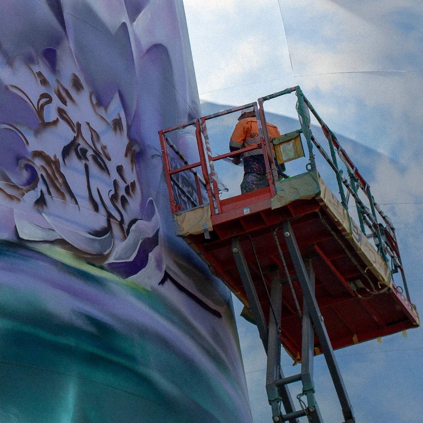 A man stands on a scissor lift to paint a silo