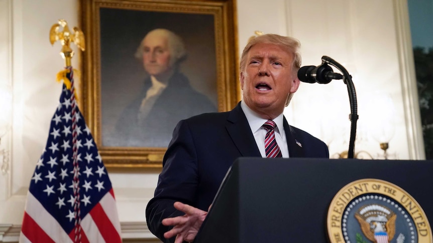 Donald Trump stands at a podium with a picture of a US president behind him