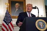 Donald Trump stands at a podium with a picture of a US president behind him