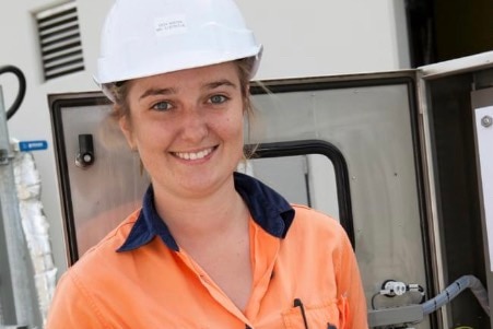 A smiling woman in a hard hat and high-vis work gear.