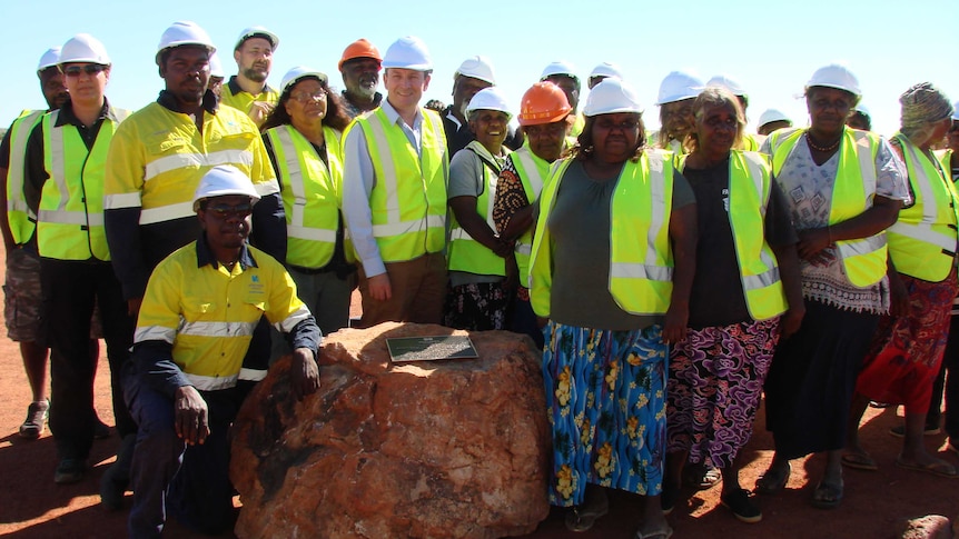 A group of people in hi-vis and hard hats stand around a plaque on a rock declaring the rare earth mine open