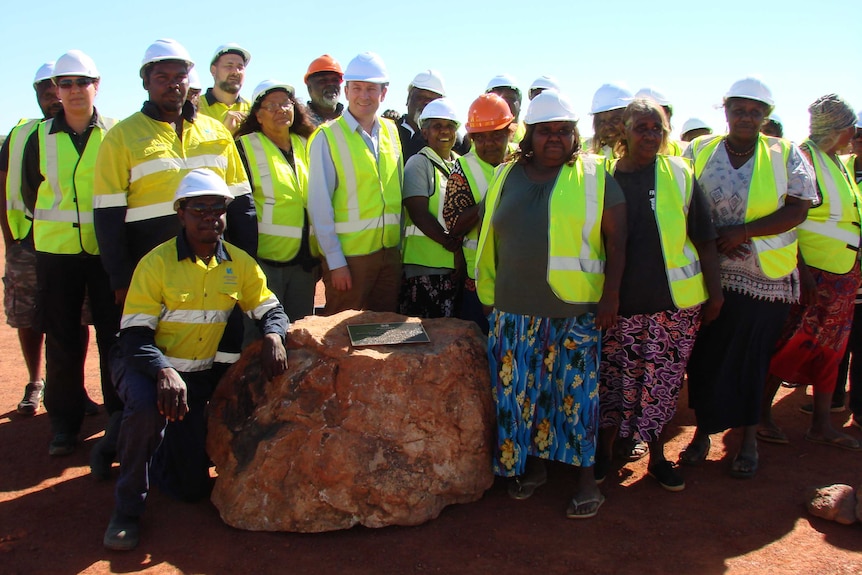 A group of people in hi-vis and hard hats stand around a plaque on a rock declaring the rare earth mine open