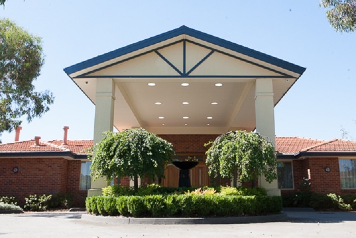A circular driveway leads up to the front door of a red-brick, single-story aged care home.