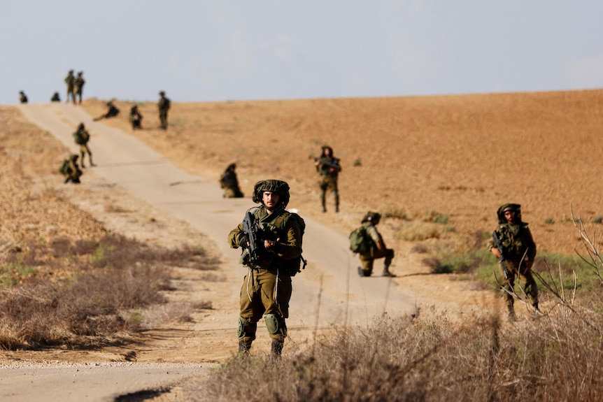 Troops stand scattered alone a dirt road.