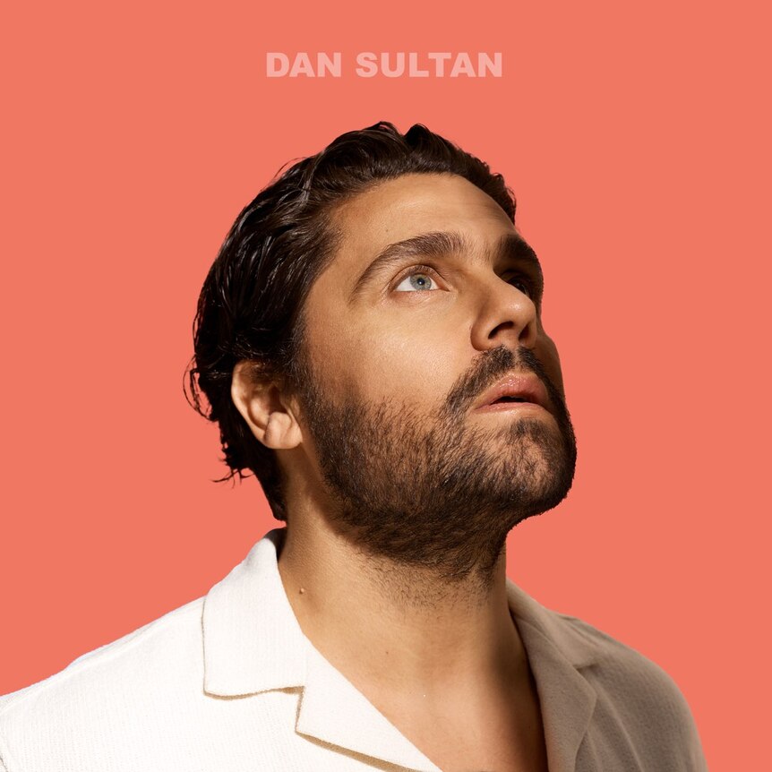 a man, dan sultan, with short beard looks up to the sky before an orange-pink background