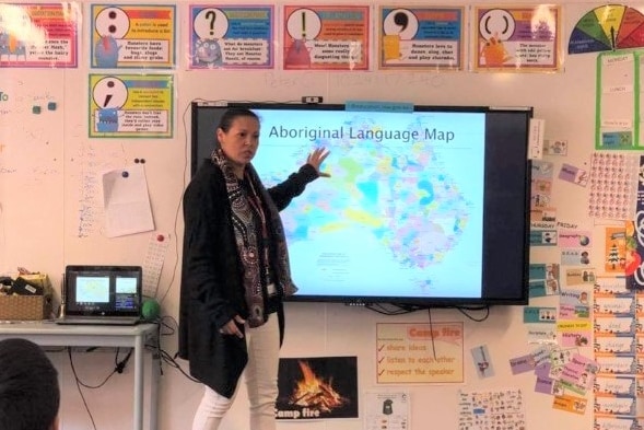 An Aboriginal woman pointing to a board teaches a classroom 
