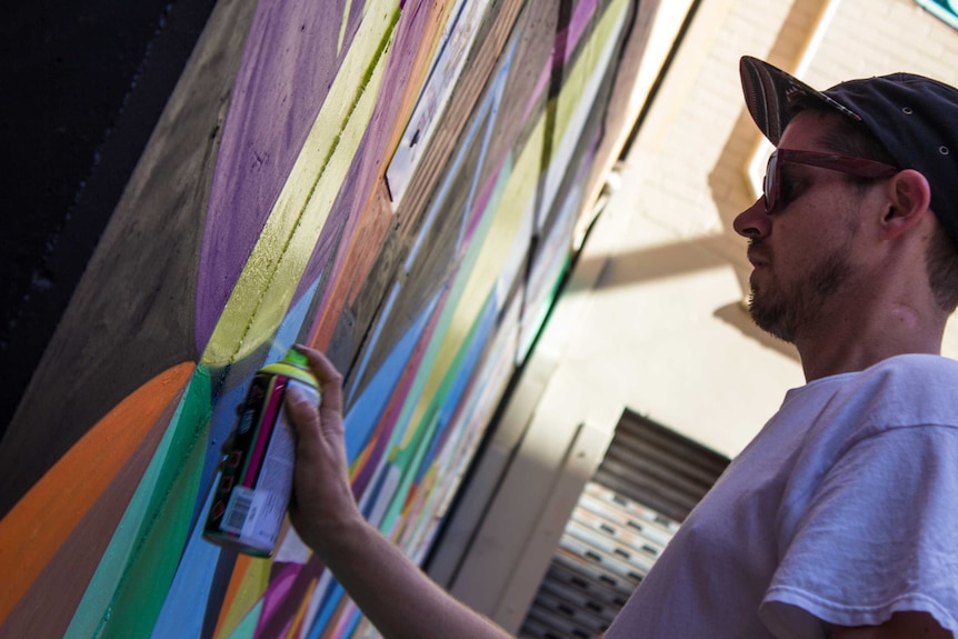 Adelaide artist Vans the Omega works in his mural in a laneway off King Street