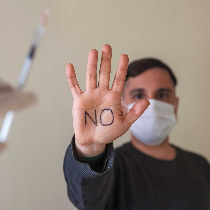 A man wearing a mask displays "no" written on his hand as he protests against getting a vaccine.