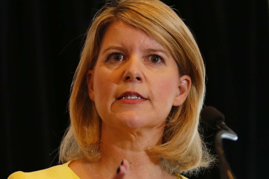 A woman in a yellow two-piece suit stands at a lectern