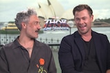 Taika Waititi and Chris Hemsworth sit laughing during press junket for new Thor film