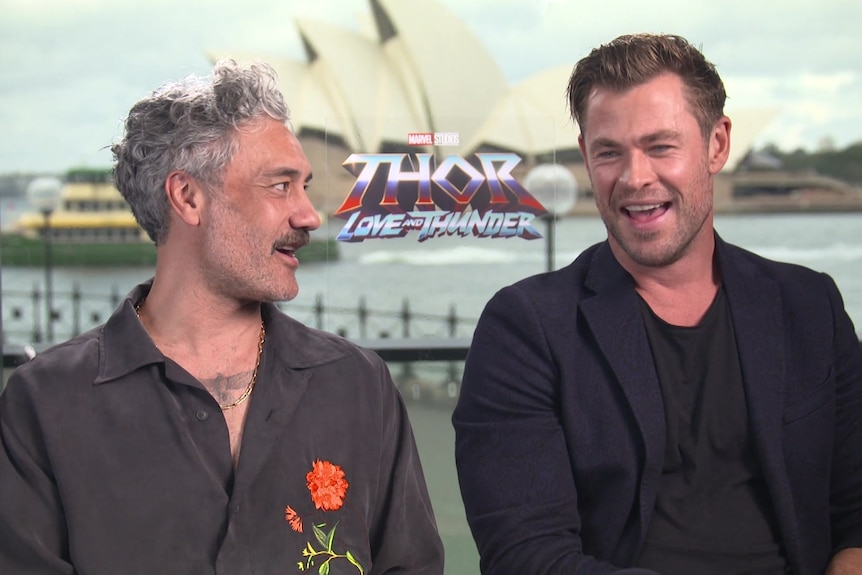 Taika Waititi and Chris Hemsworth sit laughing during press junket for new Thor film