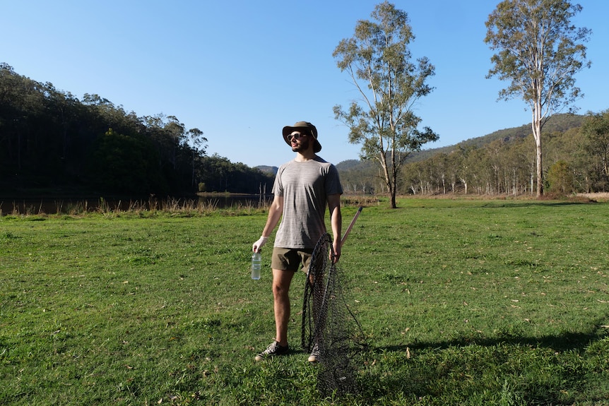 A man with a net and water bottle standing on an island in a valley