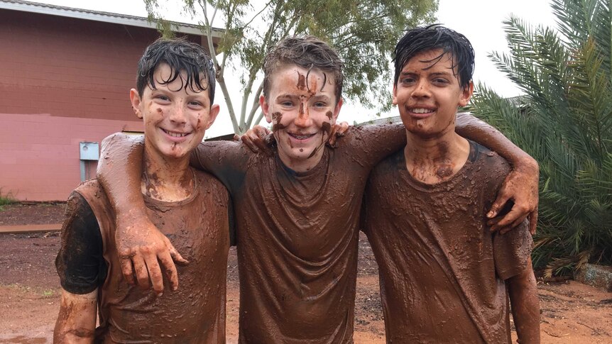 Three boys covered in mud with their arms around each other.