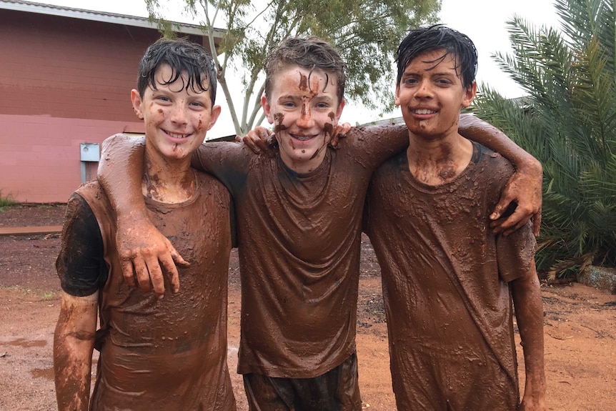 Three boys covered in mud with their arms around each other.