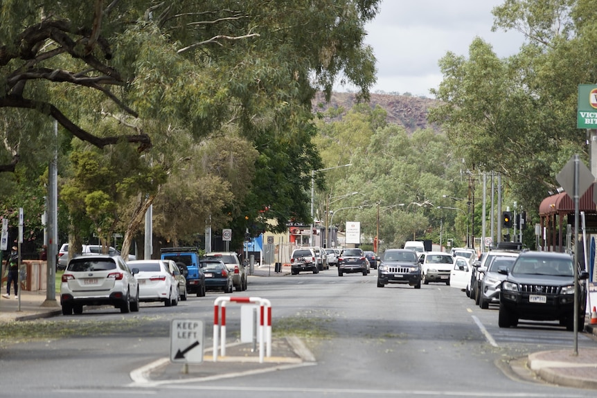 A leafy Alice Springs street with cars parked and a couple of vehicles being driven
