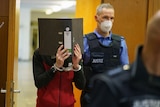 A man in handcuffs hides his face with a folder