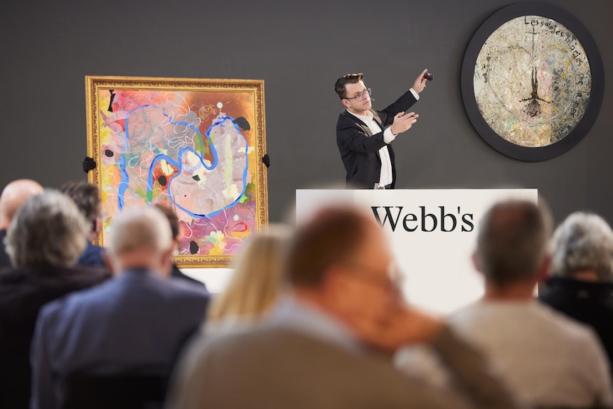 A man holds an art auction in front of a crowd of people.