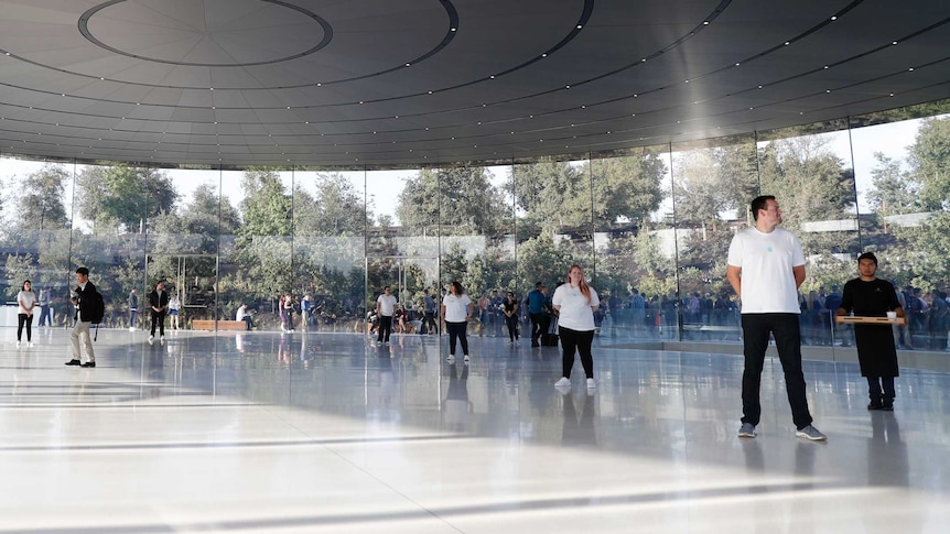 Apple staff stand watch inside the glass foyer of their new theatre as people line up outside.