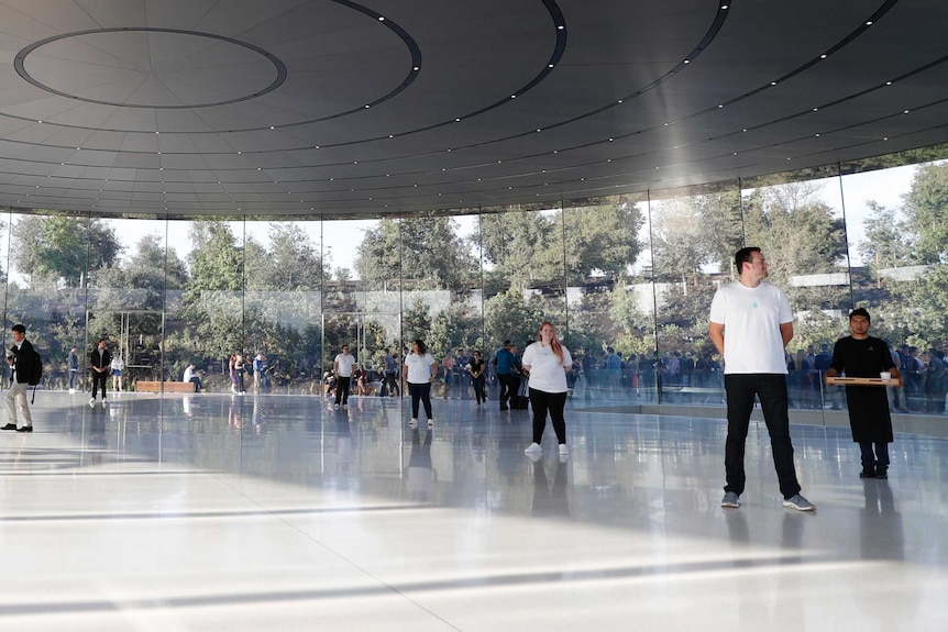Apple staff stand watch inside the glass foyer of their new theatre as people line up outside.