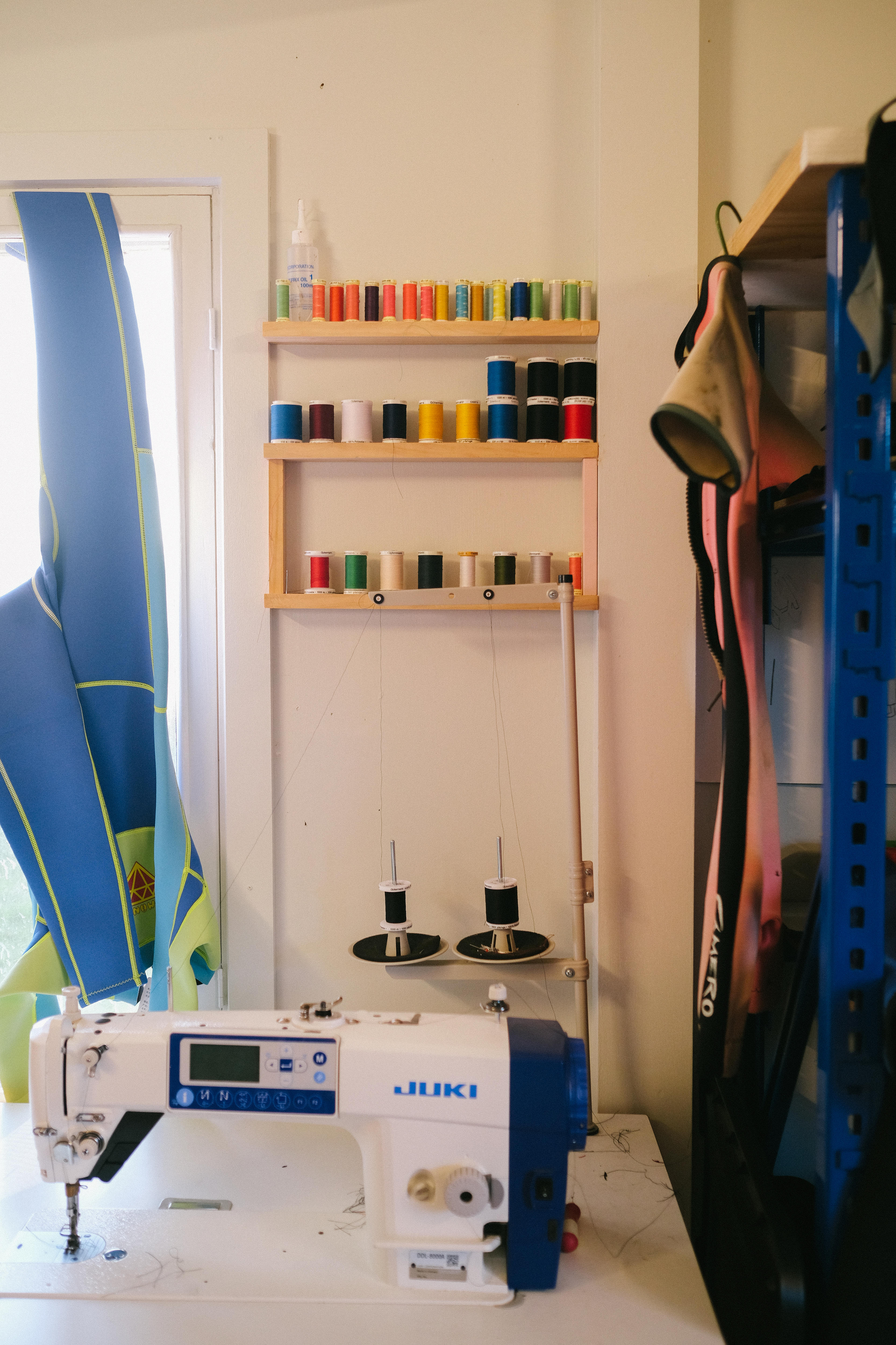 Colourful threads lines up on a wall next to a sewing machine, used for sewing the pieces of neoprene together