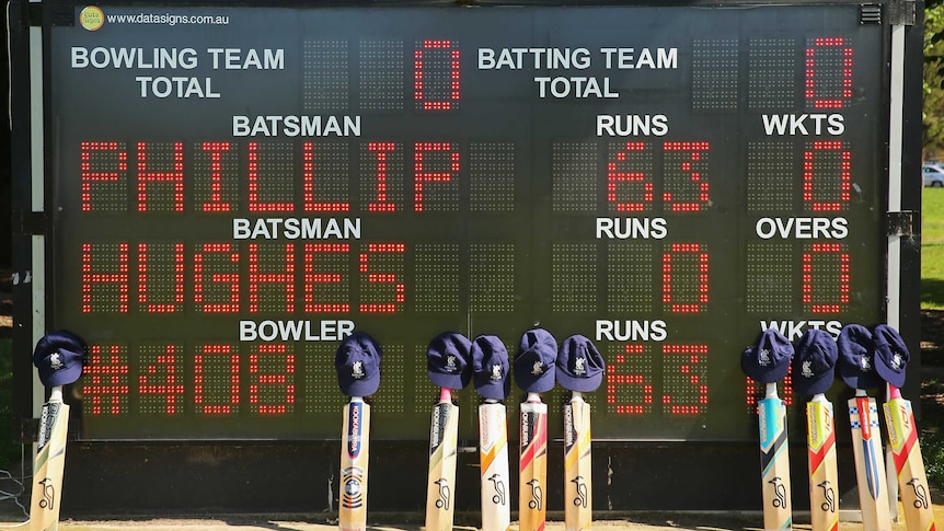 Cricket bats and caps belonging to the players are placed near the scoreboard which displays a tribute to Phillip Hughes during a match between Carlton and Fitzroy Doncaster 1st grade at Princes Park