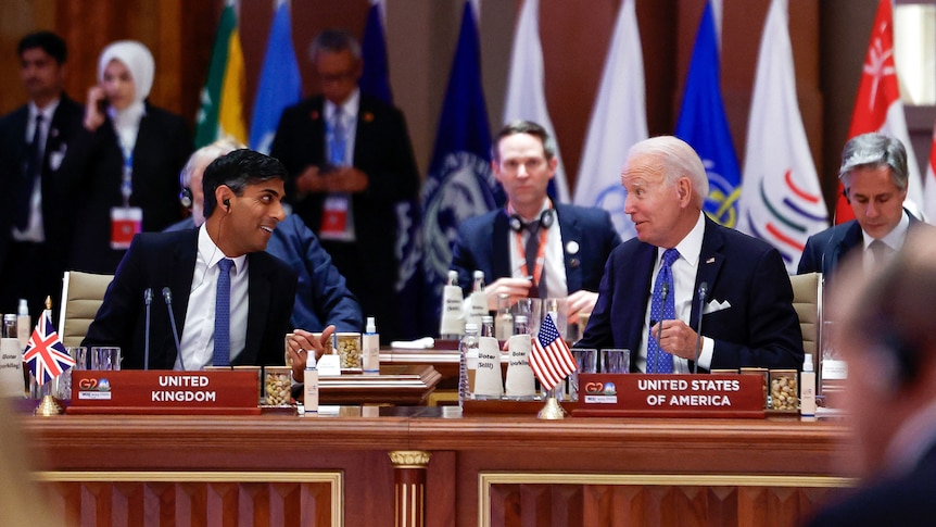 Rishi Sunak and Joe Biden sit side by side looking at eachother during a meeting.