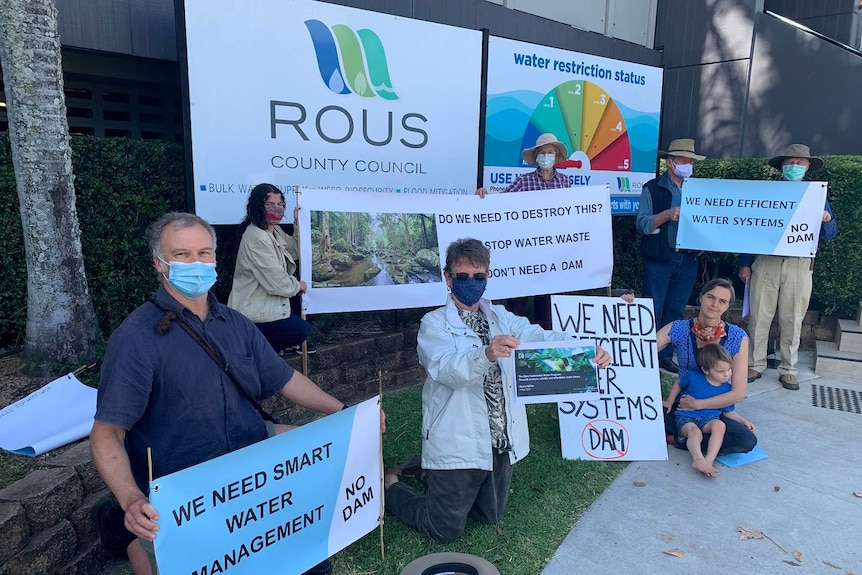 Protesters wearing COVID-19 masks hold signs opposing plans for a new dam at Dunoon outside the office of the Rous County Counci