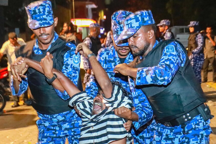 Three Maldivian police officers drag a protester away.