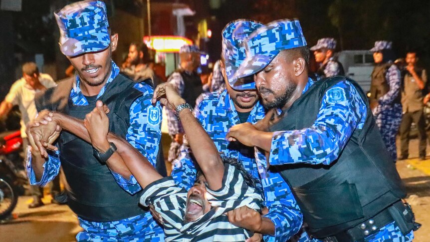 Three Maldivian police officers drag a protester away.