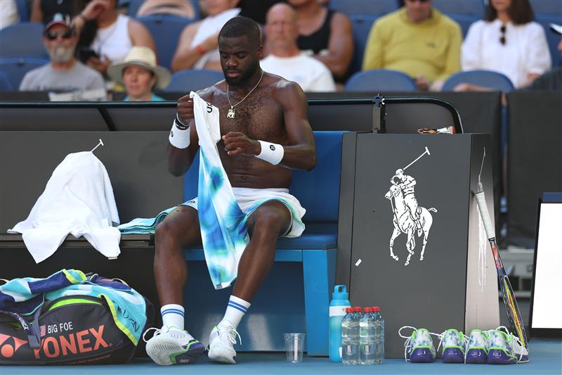 El tenista Frances Tiafoe se sienta sin camisa al margen y con botellas de agua a sus pies.