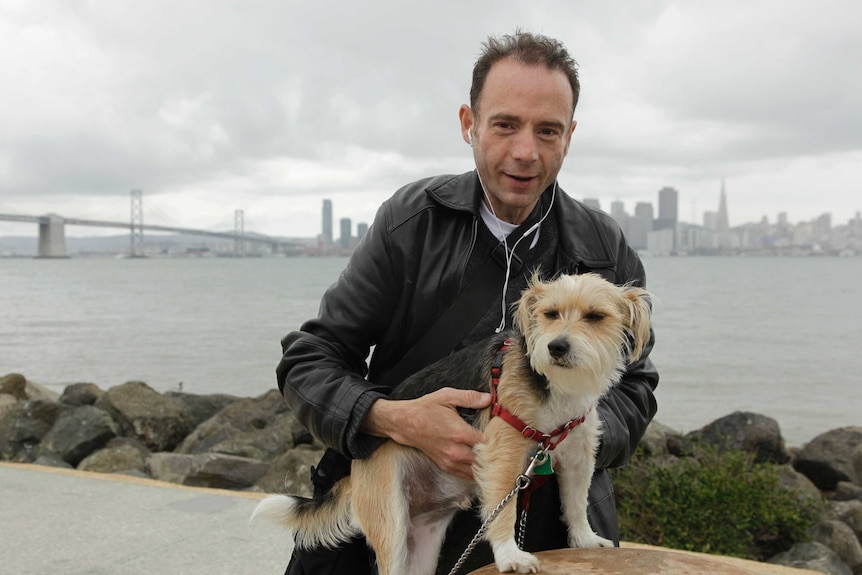 A man poses for a photo with his dog and the San Francisco city is in the background