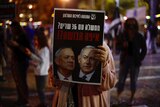 a protester hold up a poster with Netanyahu and Gantz's faces in shadow