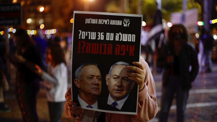 a protester hold up a poster with Netanyahu and Gantz's faces in shadow
