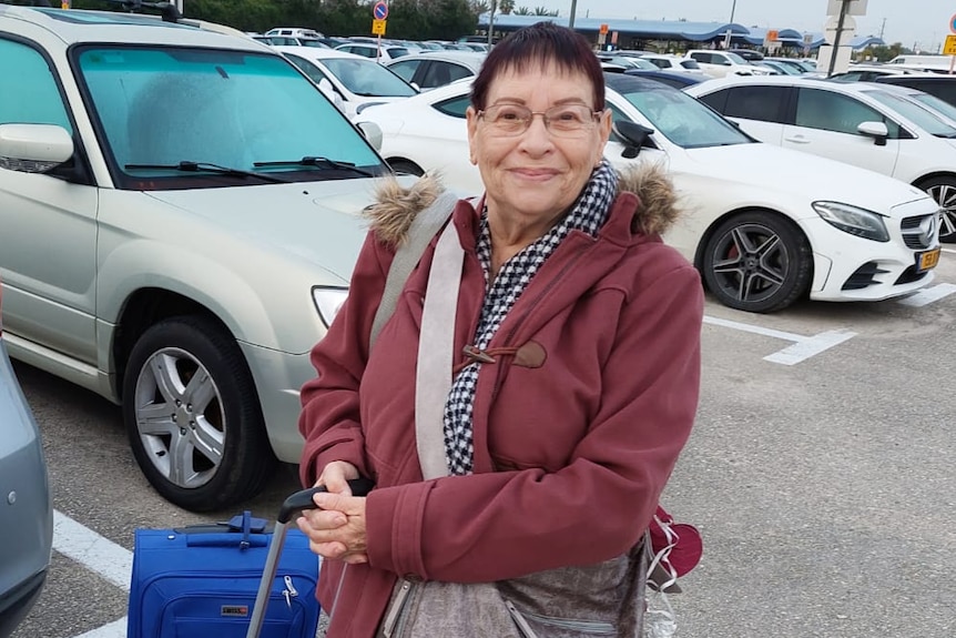 A woman stands in a carpark next to luggage, smiling at the camera