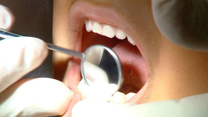 TV still of close-up of open human mouth with dentist examining teeth with dental mirror instrument in October 2008.