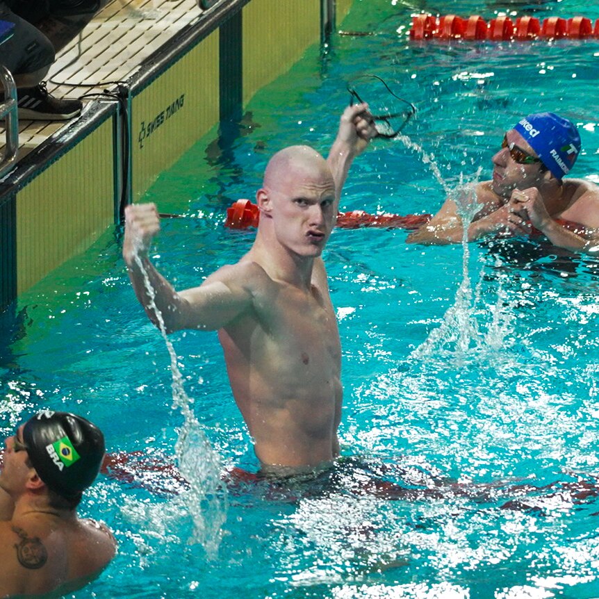 A male para-swimmer pumps his fists in the pool after winning a race