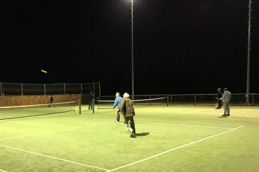 men playing tennis court at night under lights