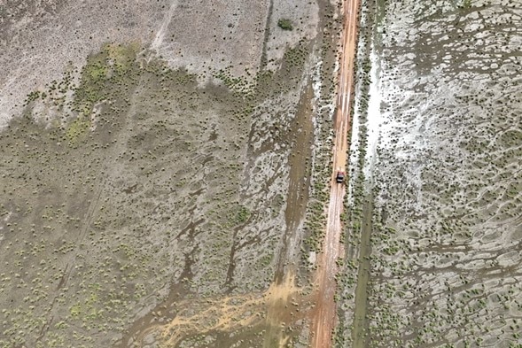 A drone shot of a vehicle travelling down a flooded road