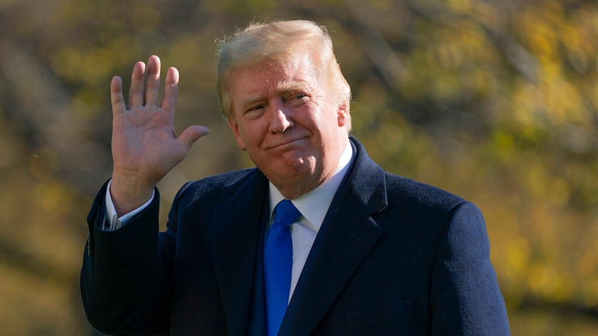 President Trump, dressed in a blue suit and tie, waves and gives a small smile.